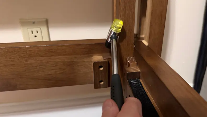 Wooden joinery bed frame shown being assembled using a yellow-tipped rubber mallet.
