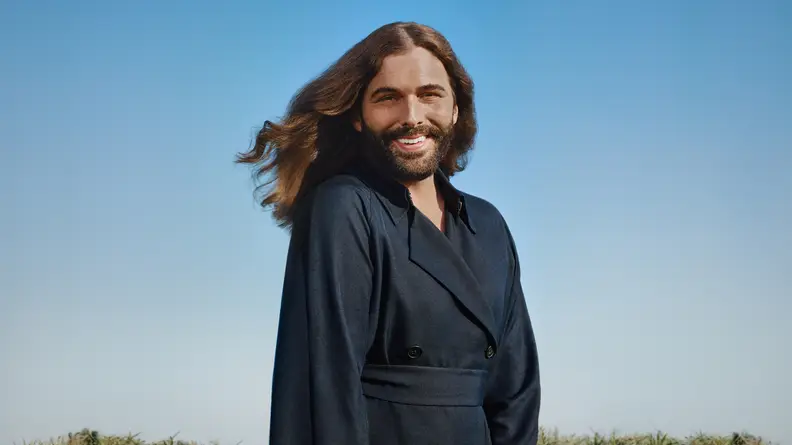 Jonathan Van Ness stands against a sky in the background.
