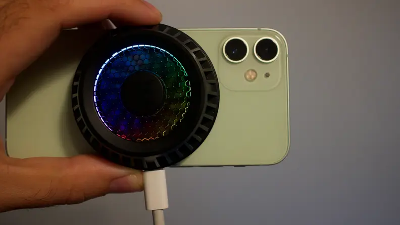 A close-up of the fan attached to the back of an iPhone 12 Mini, while also plugged into a charging cable.