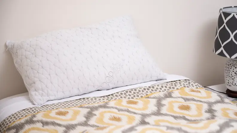 the coop home original pillow on a bed with a yellow blanket