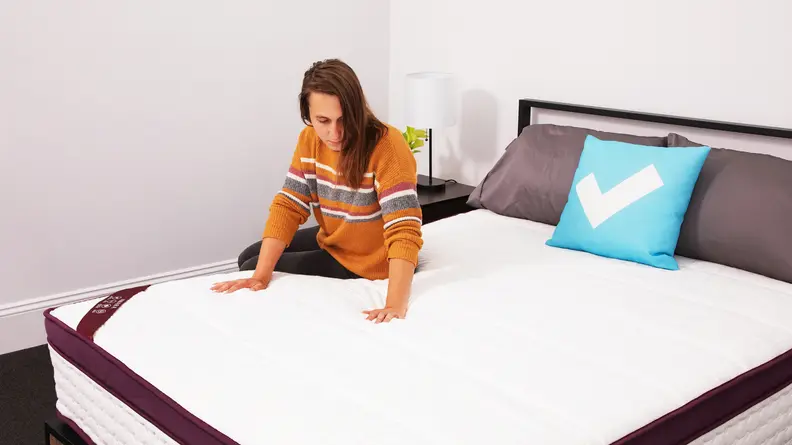 A person sitting on the Awara Premier Natural Hybrid Mattress and pressing their hands into the cover.