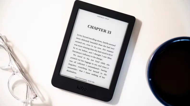 Black e-reader on white surface next to reading glasses