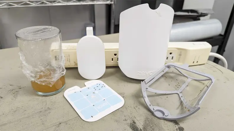 The Zevo Flying Insect Trap with a tape strip with dead flies on it and a jar of brown liquid.