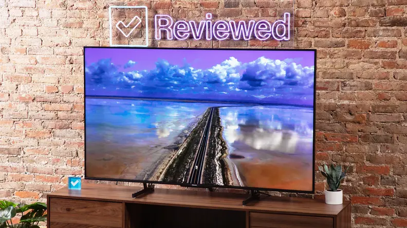 Hisense U7K Mini-LED TV sitting on top of wooden television stand in front of brick wall and Reviewed LED sign.