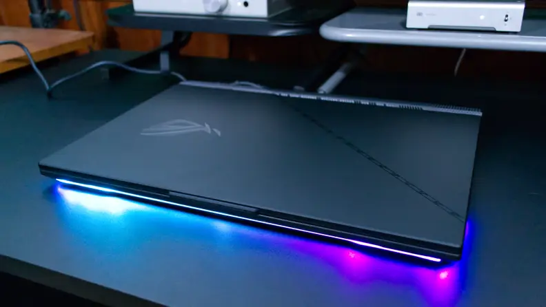 The Asus ROG Strix SCAR 17 (2023) closed, as the keyboard illuminates on a desk. .