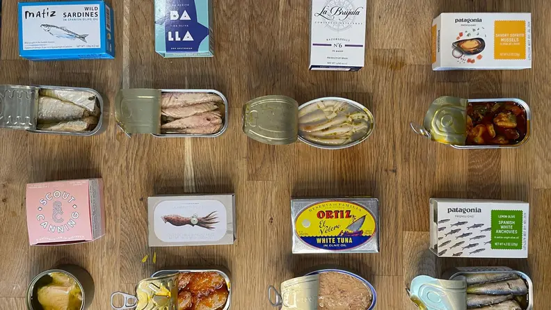 Assorted tinned fish and conservas arranged on a wooden table.