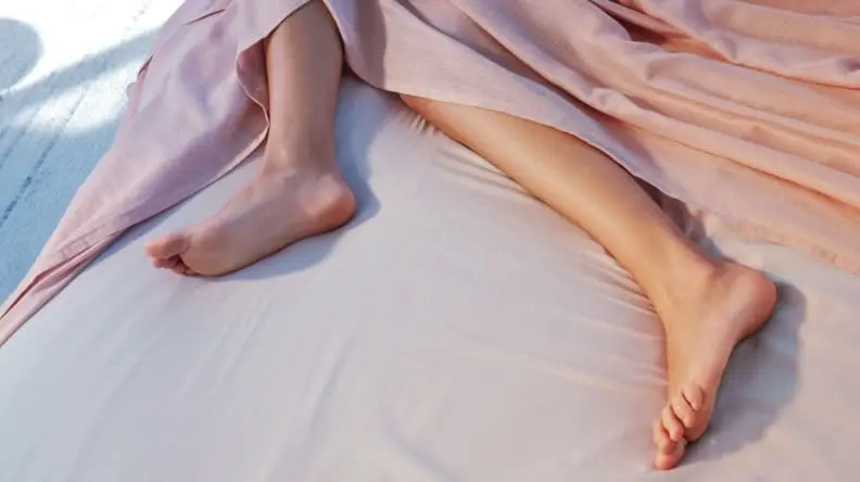 someone's legs and feet protrude from beneath the Casper Hyperlite sheets in dusty rose
