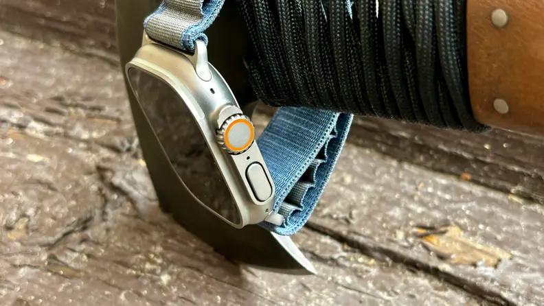 An Apple Watch Ultra 2 hangs from the handle of a hatchet. Very outdoorsy.