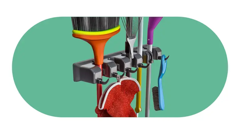 A dust pan, a broom and a small rake being held within a vertical wall mount.