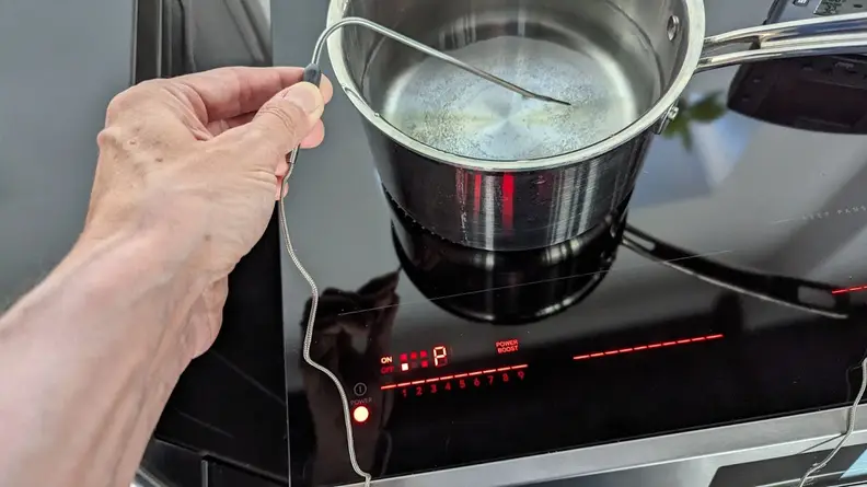 Person holding corded slim thermometer within pot with boiling water on the cooktop of the Frigidaire Gallery GCFI3060BF 30-inch Induction Range.