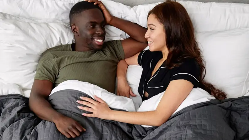 a man and woman in bed talking beneath a gray gravity blanket