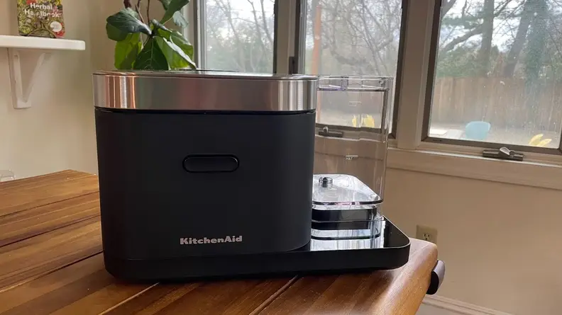 Navy blue KitchenAid Grain and Rice Cooker sitting on wooden countertop in front windows.