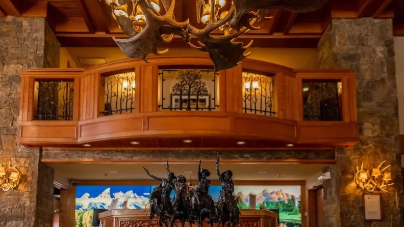A beautiful, rustic check-in area showing a mini sculpture of four cowboys on the desk and antler lighting fixture above it