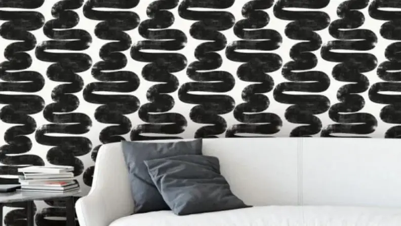 Black wavy lines are against a white background make up this wallpaper that's pasted on the walls behind a white couch.