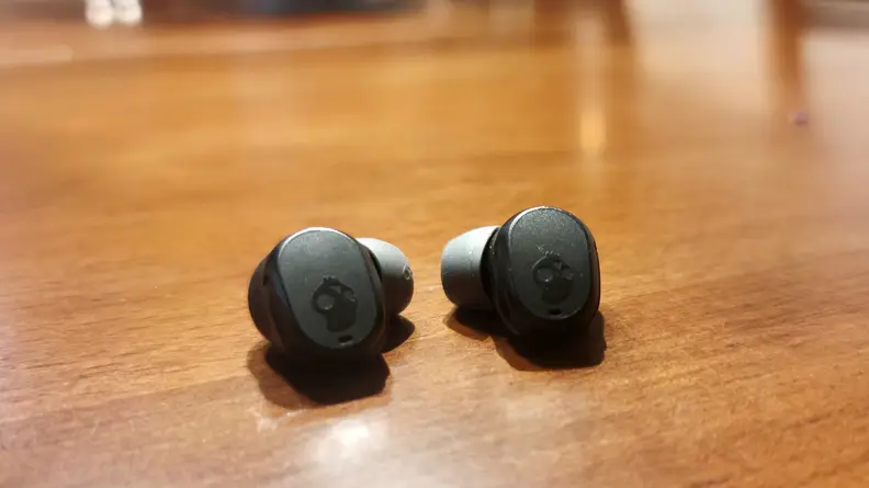 The all-black Skullcandy Mod earbuds sit on a wooden cabinet