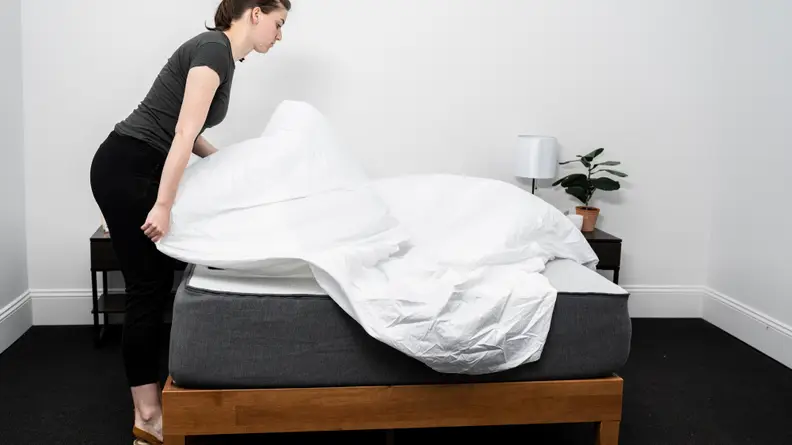 a woman spreads a sheet over the Casper Select mattress