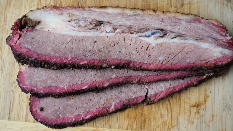 Three slices of smoked brisket on wooden surface.