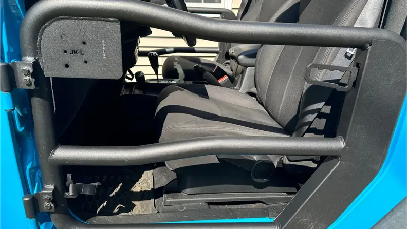 Close-up view of a black Rugged Ridge Fortis Tube Door installed in a light blue Jeep.