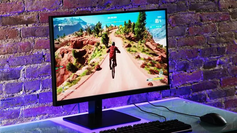 Destop monitor with animated game on screen in front of brick wall sitting on top of desk with keyboard and mouse.