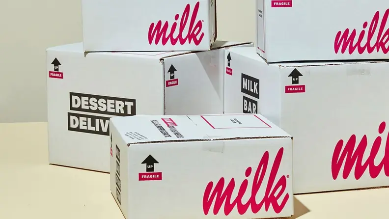 A stack of white cardboard boxes with pink cursive on the sides that read, "milk."