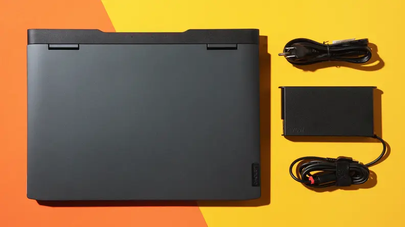 The Lenovo IdeaPad Gaming 3 laptop next to USB cords and charger, on an orange background.