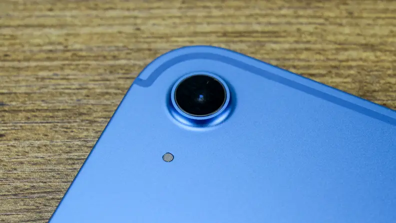 The blue Apple iPad 10 sits on a wooden desk with its back camera in view.