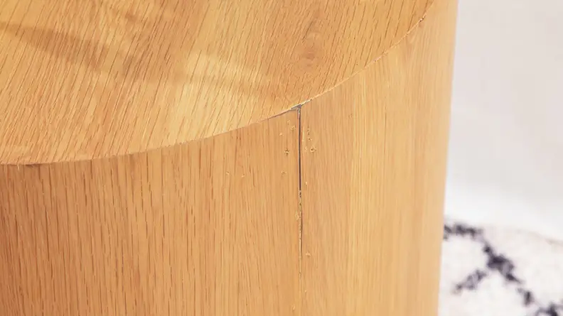 A close-up of a wood side table focused on a split in the veneer.