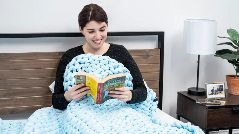 a person reading under the Nuzzie weighted blanket