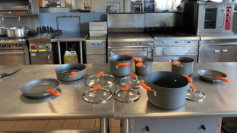 Rachael Ray's 14-piece cookware set arranged neatly on a stainless steel kitchen workspace.