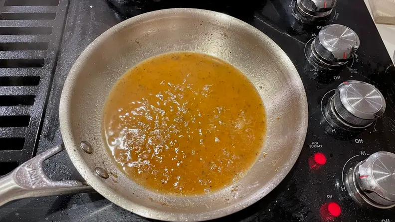Leftover fond inside a stainless steel pan on a black stovetop.