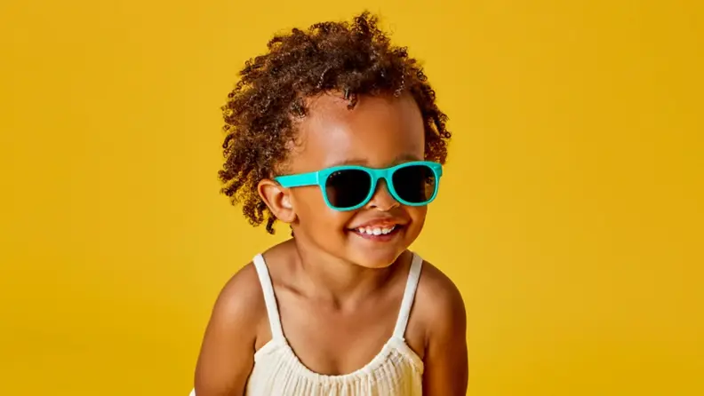 An adorable Black girl smiles at the camera in her teal sunglasses