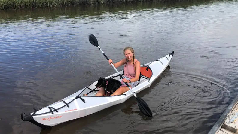 A woman uses an Oru Kayak Beach LT Foldable Kayak in the water, and it could be one of the best birthday gifts for Aries season.