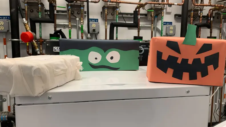 Four boxes adorned with construction paper. From left to right, they look mummified, like a Frankenstein's monster, and like a carved Jack-o'-Lantern.