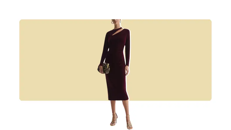 A model wearing a form-fitting red velvet dress with a cutout detail along the neckline. She holds a purse.