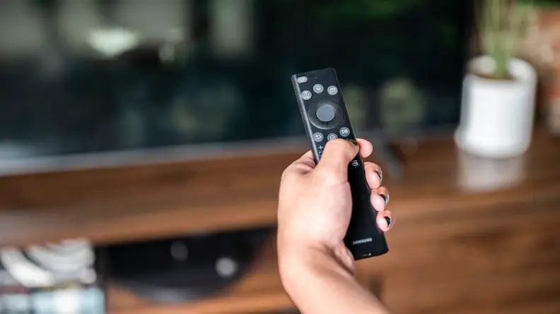 A close-up of someone's hand holding the Samsung Solar Remote in front of the Samsung Q60B