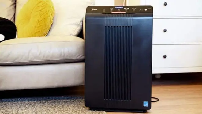 Black air purifier on floor next to couch.