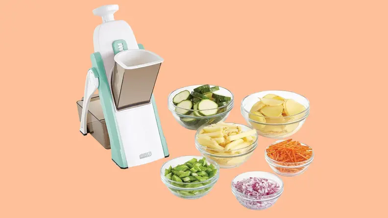 Dash Mandoline surrounded by bowls of sliced vegetables on an orange background