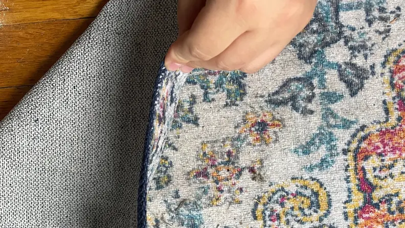 A hand lifting and folding a corner of the rug.
