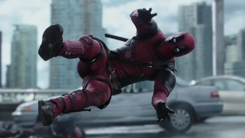 Deadpool (Ryan Reynolds) being launched into a car with a city skyline in the background.
