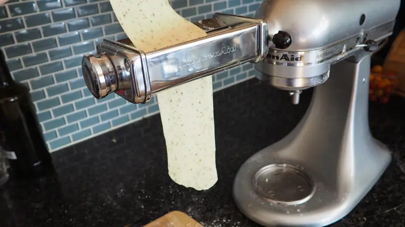 Dough is fed through the slot of a KitchenAid pasta attachment.
