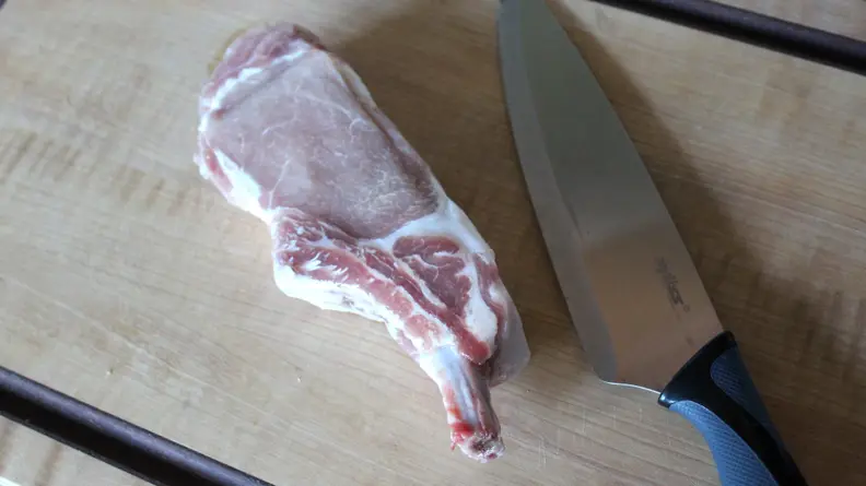 In the center of the cutting board, there's a piece of uncooked Kurobuta pork chop and a knife.