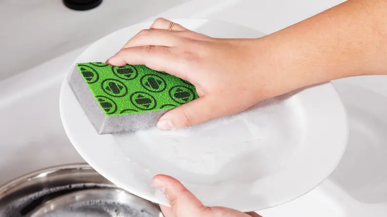 Person using the Skura Sponge to clean plate in sink.