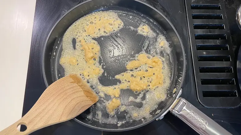 A wooden spoon in a Joseph Joseph cooking pan that is being cleaned.