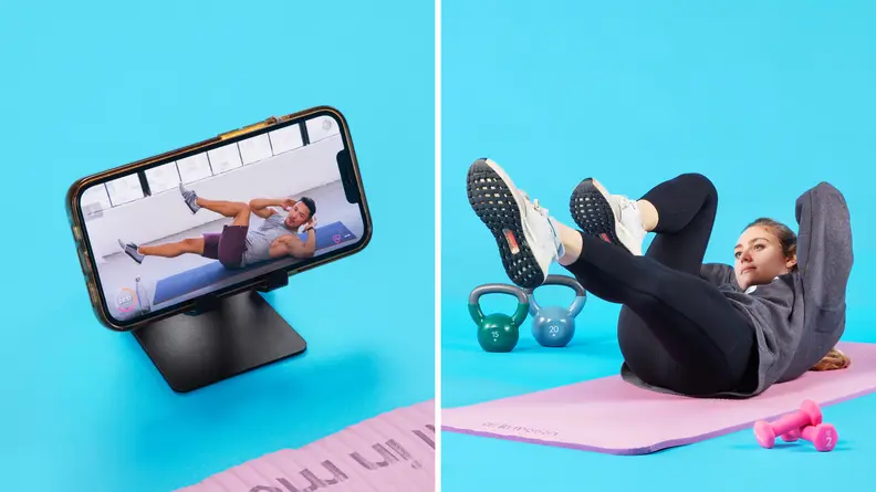 On left, smart phone perched on phone stand with FitOn app on screen. On right, Person laying on yoga mat with feet elevated in the air and arms behind head completing a workout.