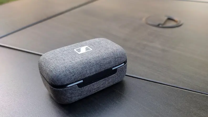 The grey fabric Sennheiser Momentum True Wireless 3 case sits on a black table.