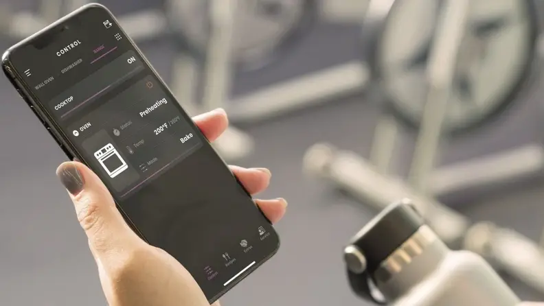 A person hold a smart phone in their hand and the screen displays the SmartHQ app in use.