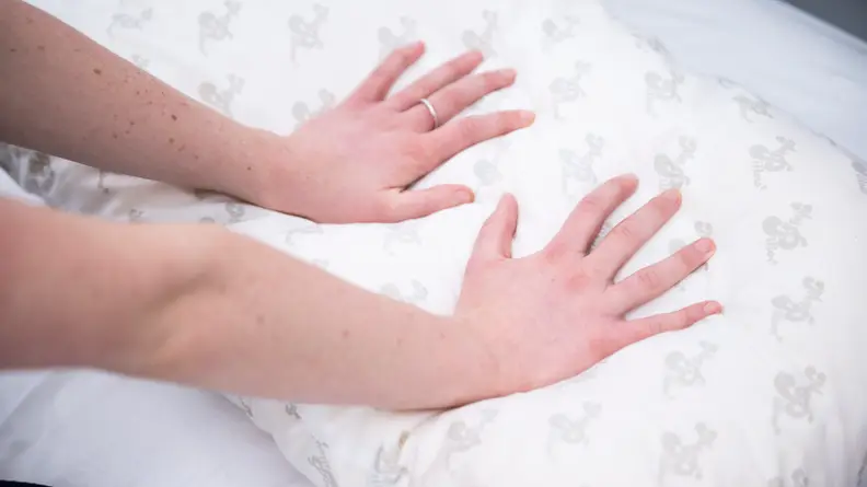 A pair of hands pressing down on a pillow.