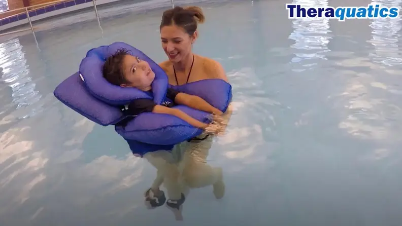A boy wearing a floatie in the water with the support of his mother.