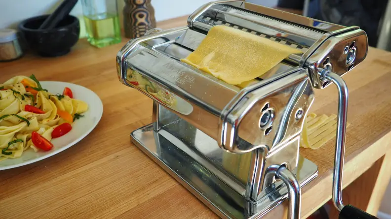The Marcato Atlas pasta maker sits on a kitchen counter with a piece of dough in its slots.