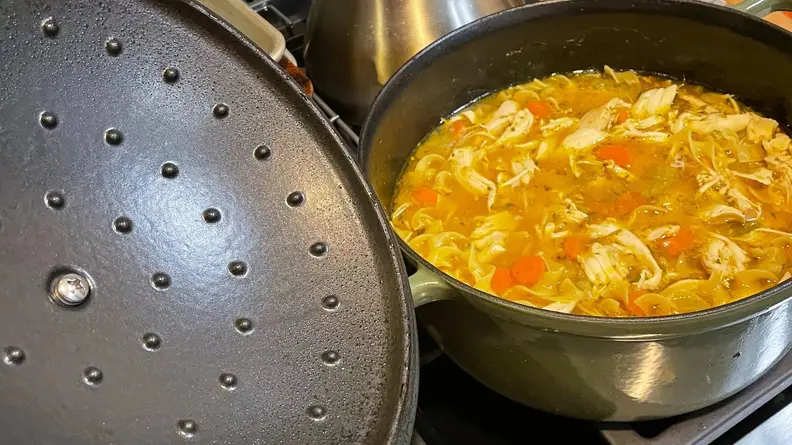 Chicken noodle soup with assorted vegetables inside of pot on stovetop.